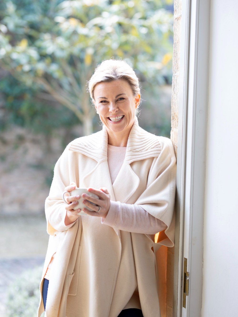 Katie Brindle in a cream cardigan holding a drink