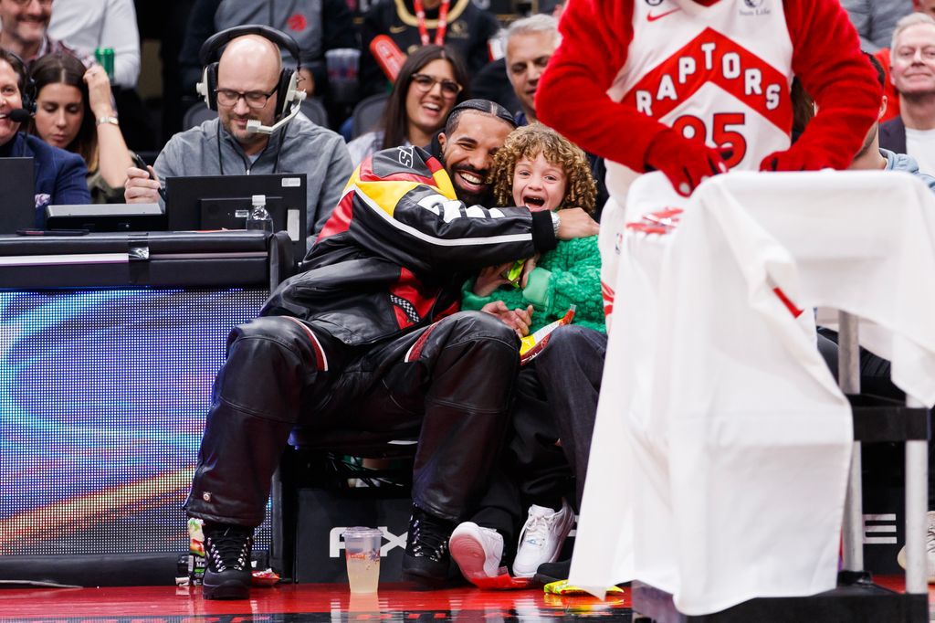 Drake embraces his son Adonis as the Raptor mascot brings over candy for him during the first half of the NBA game between the Toronto Raptors and the LA Clippers at Scotiabank Arena on December 27, 2022 in Toronto, Canada