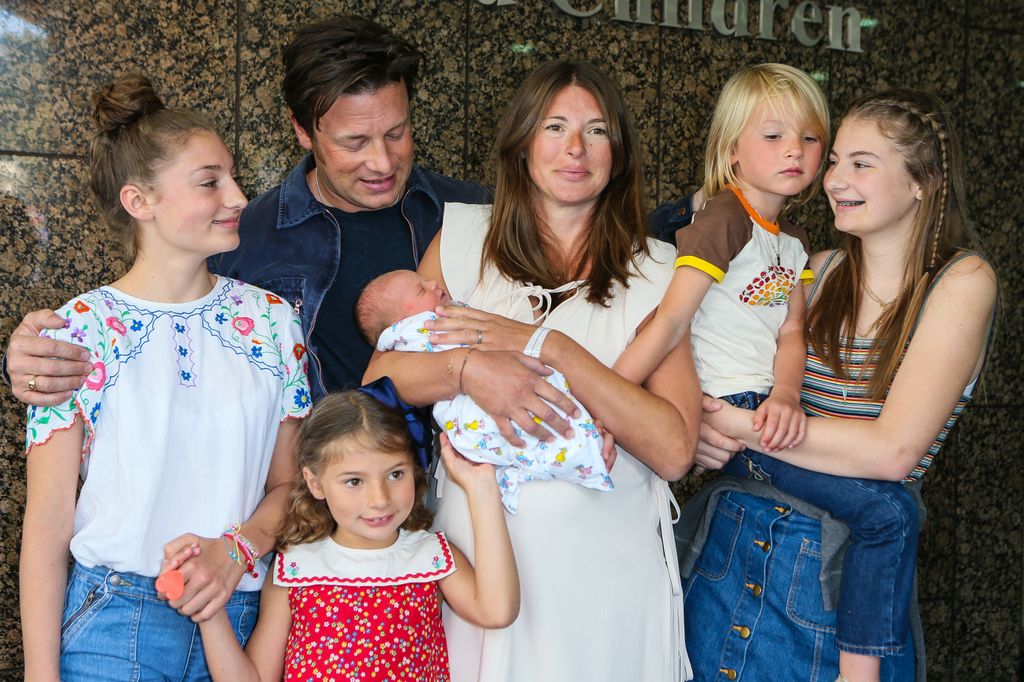 Jamie Oliver and Jools Oliver and children posing with youngest child outside Portland Hospital