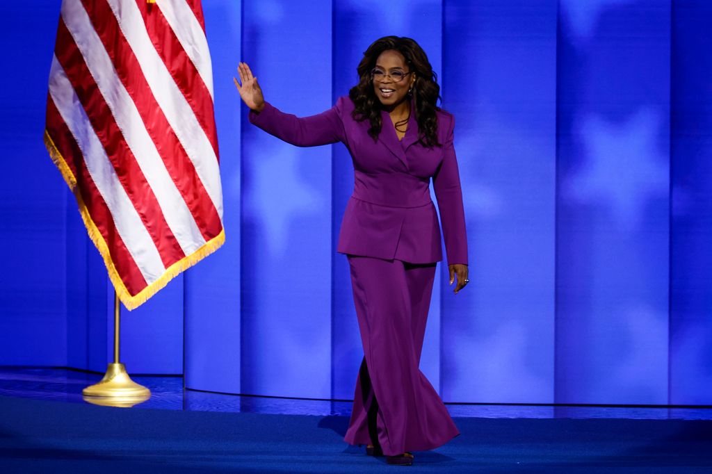 Oprah Winfrey on stage waving in a purple power suit