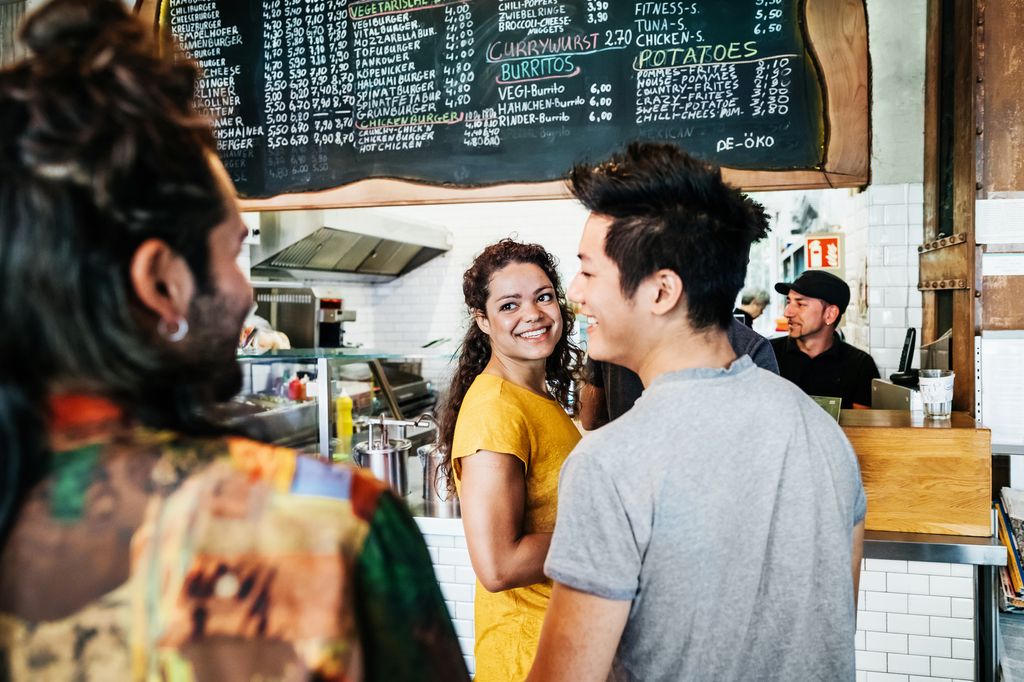 A group of friends chatting while waiting in line to order some food at a trendy burger restaurant.