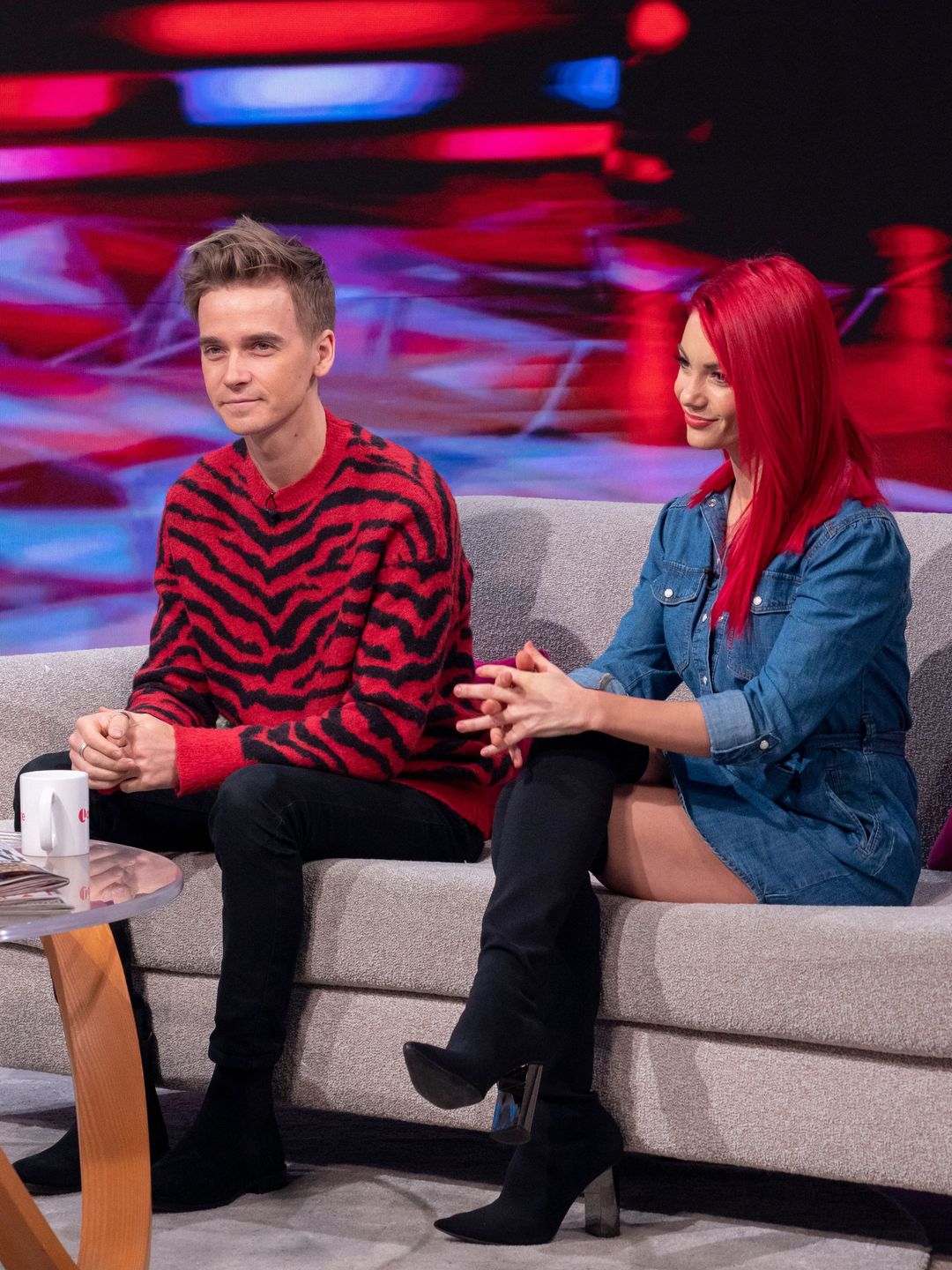 Joe Sugg and Dianne Buswell sitting on a sofa with straight faces