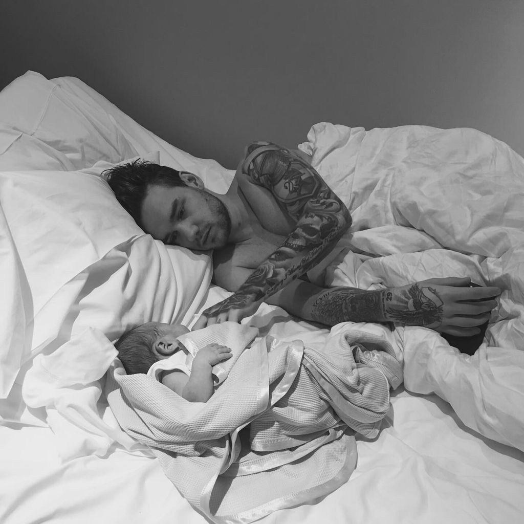 Liam Payne shirtless lying in bed with white sheets with baby son Bear 