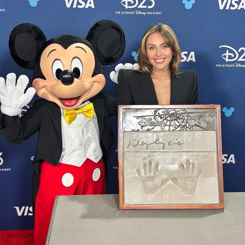 Miley Cyrus poses with Mickey Mouse and her handprints after being honored as a Disney Legend at D23 2024