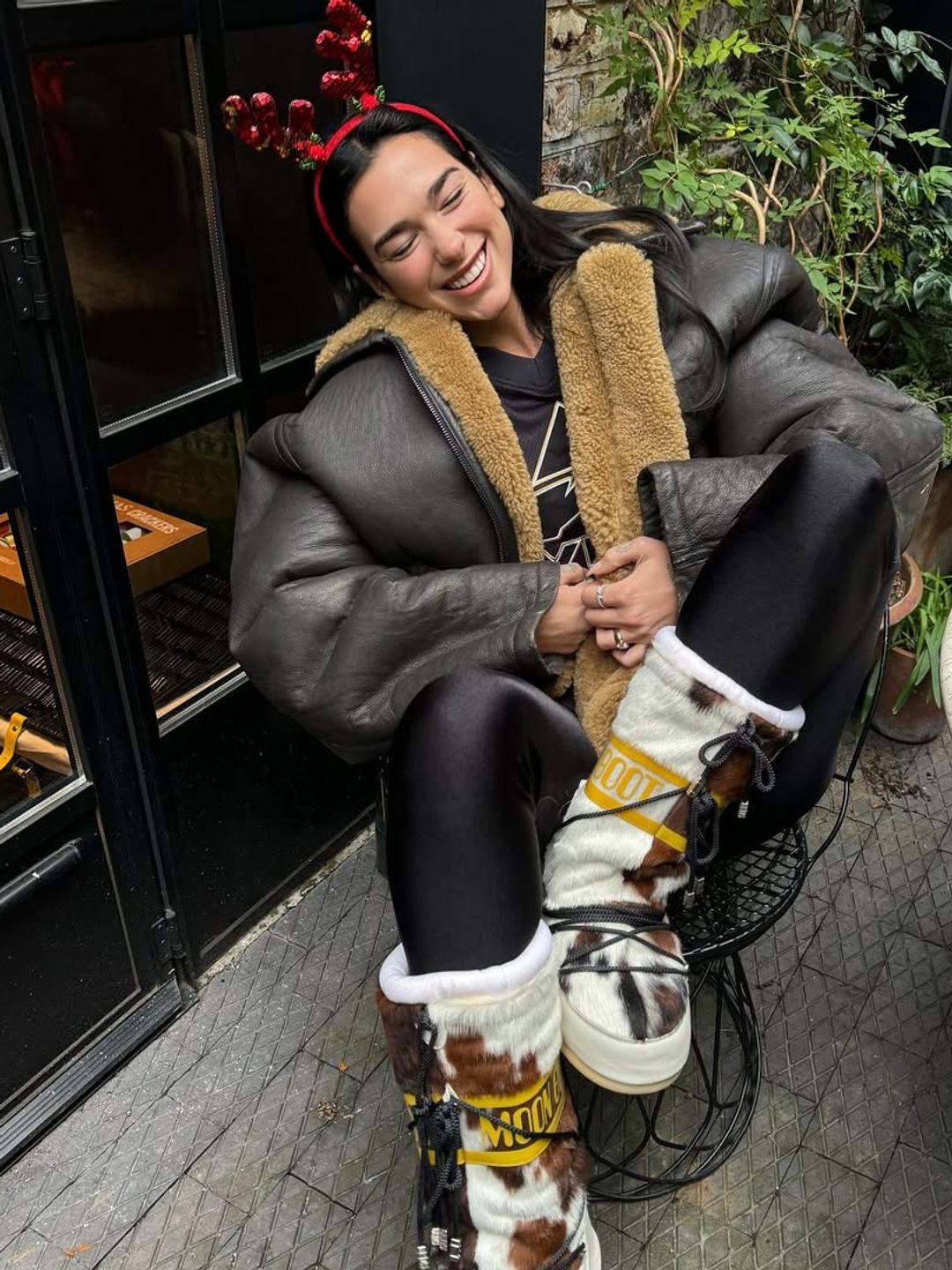 Dua Lipa's antlers, cow print snow boots, and leather jacket merge festive whimsy with functional, edgy style.