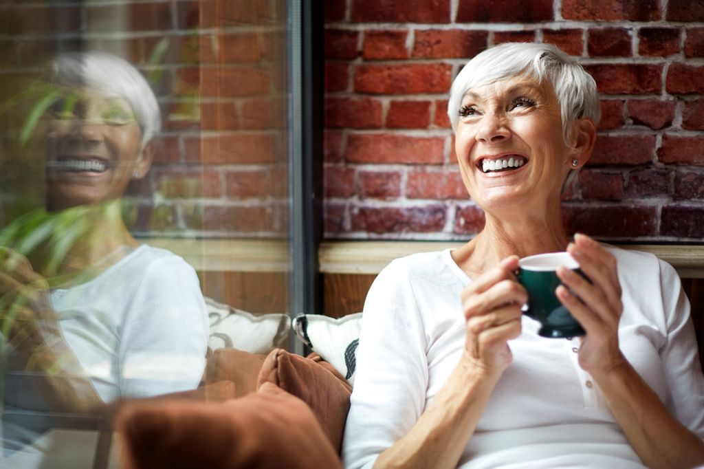 Beautiful elderly woman fondly recollecting while drinking a hot drink from a cup.