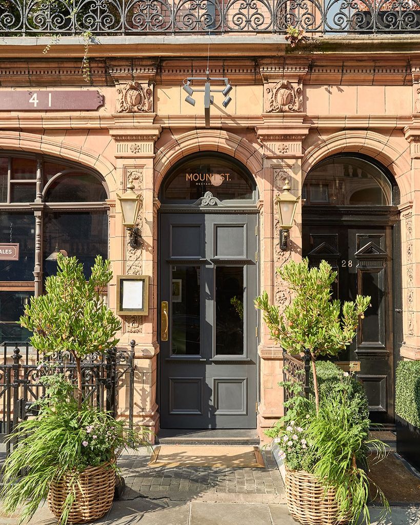 outside of restaurant with brick exterior and plants by grey door