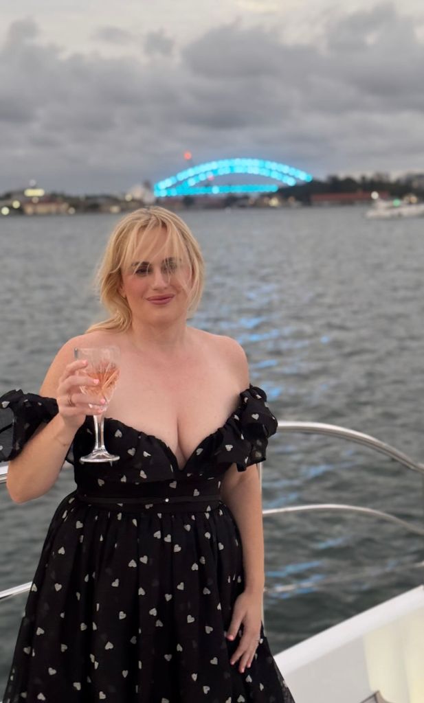 Rebel Wilson on a party boat wearing a dress covered in hearts