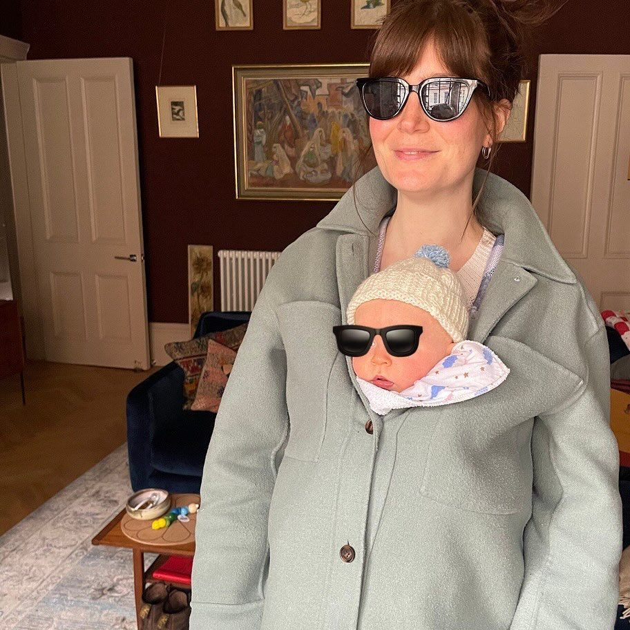 Natasha in her living room with baby in her coat