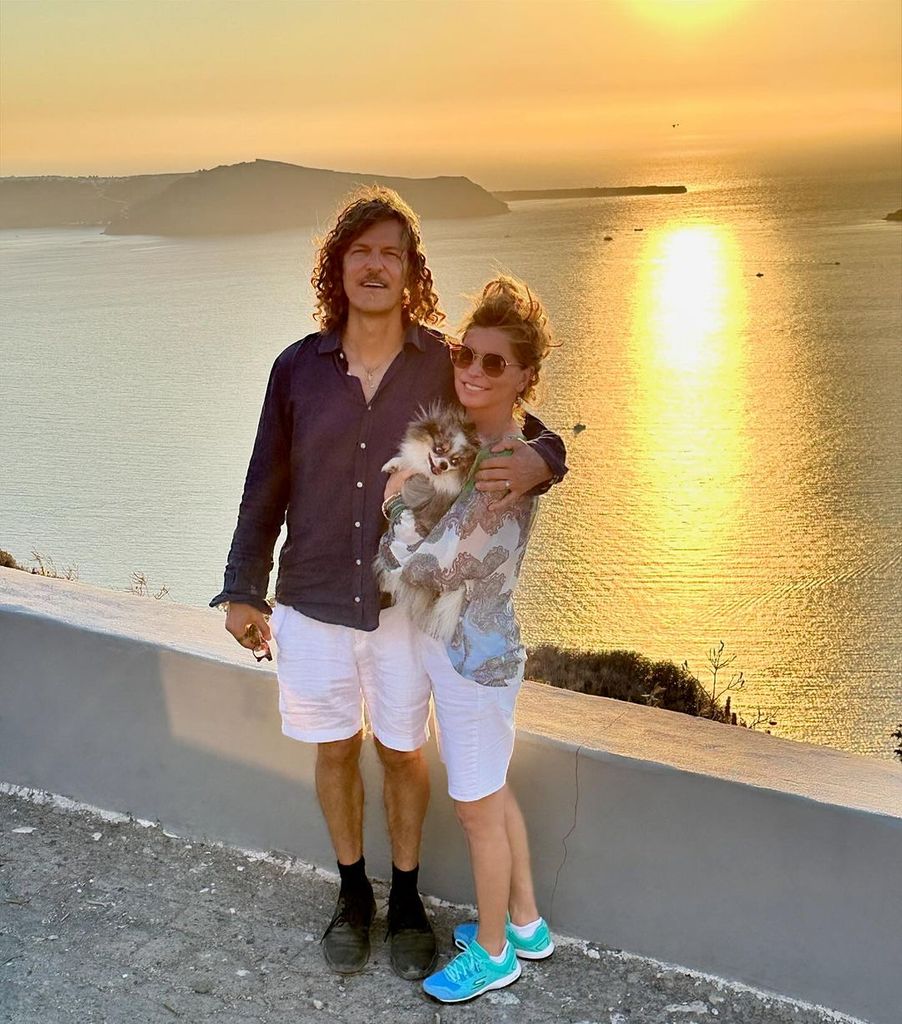 Shania Twain holds her dog Sapphie as she poses with husband Frederic Nicolas Thiebaud in front of sunset