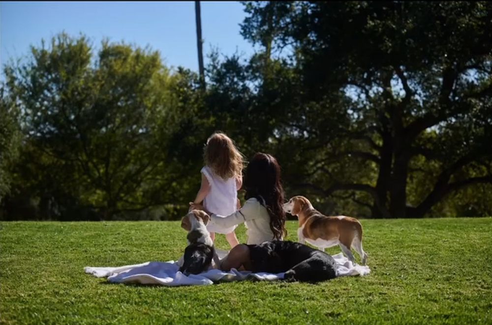 Princess Lilibet and Meghan Markle are seated on a blanket surrounded by their three dogs