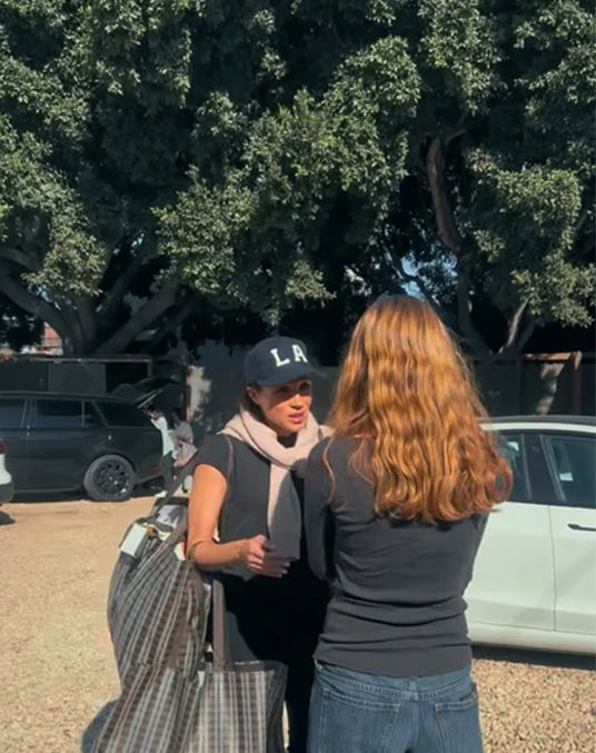 Meghan Markle in a t-shirt and cap talking to a woman