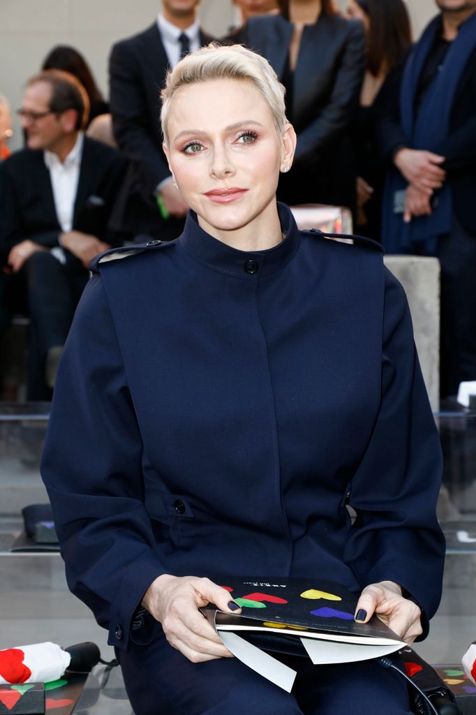 Princess Charlene wearing a navy suit whilst holding a programme at Paris Fashion Week