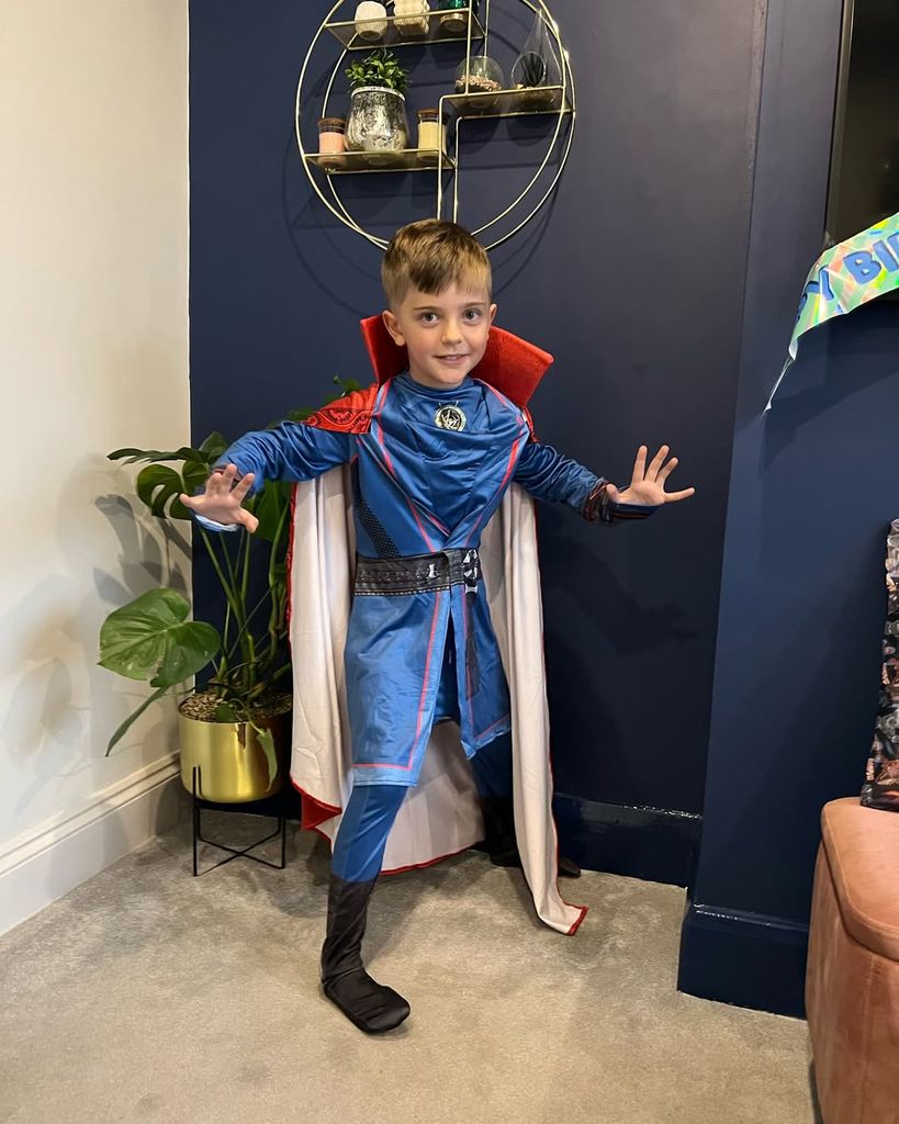 Izzi Warner's son poses for photo in a fancy dress costume while standing in the family living room