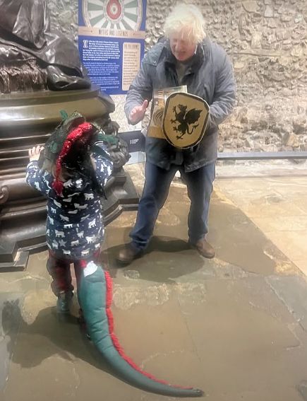 A young child dressed as a dragon plating with Boris Johnson holding a shield