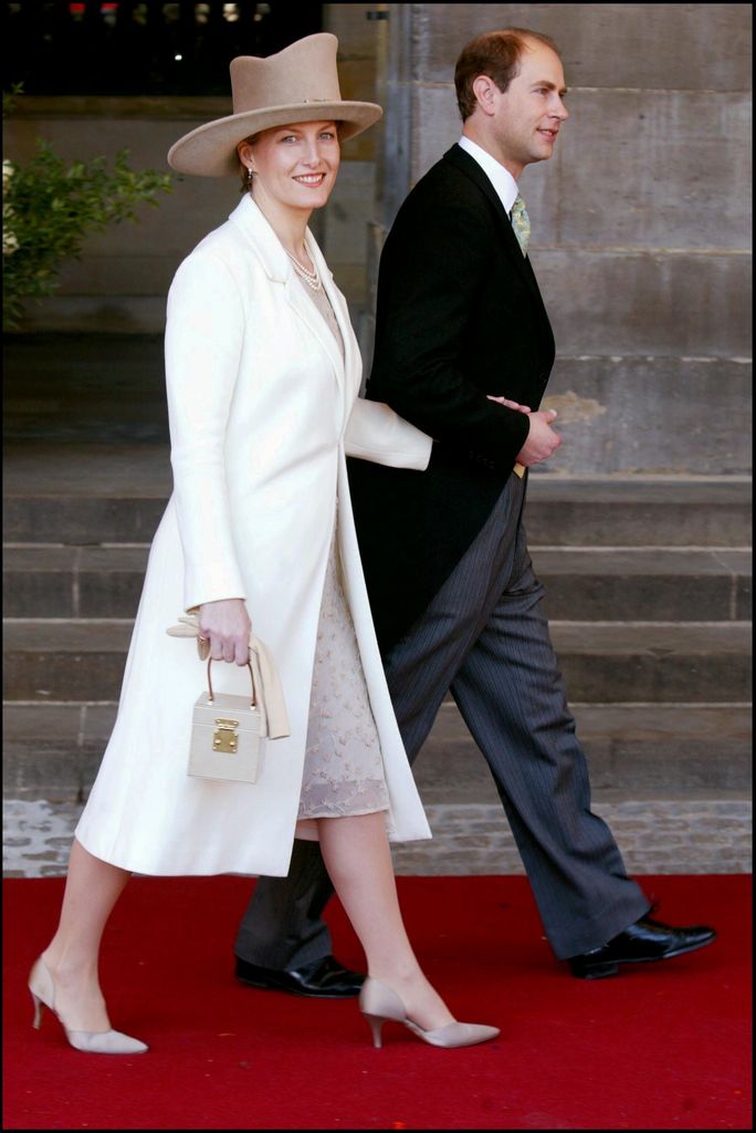 Duchess Sophie in a white jacket and beige hat with her arm in Prince Edward's