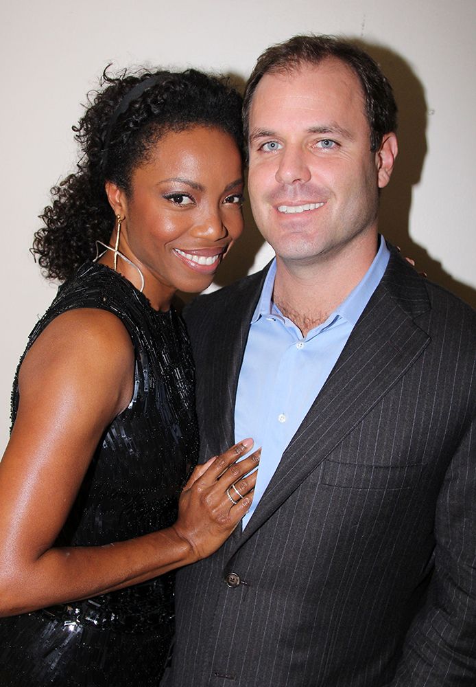 Heather Headley and Brian Musso cuddle up. She is wearing a black dress and he is wearing a black suit jacket and pale blue shirt