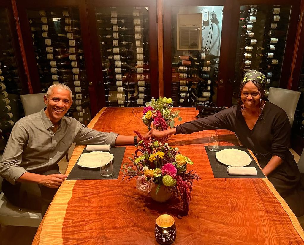 Barack and Michelle Obama hold hands over a dinner table set for two