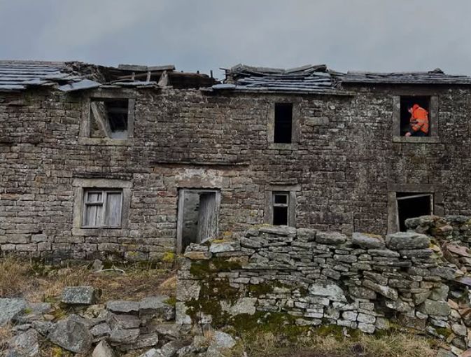 Reuben Owen in an orange vest inside a derelict cottage