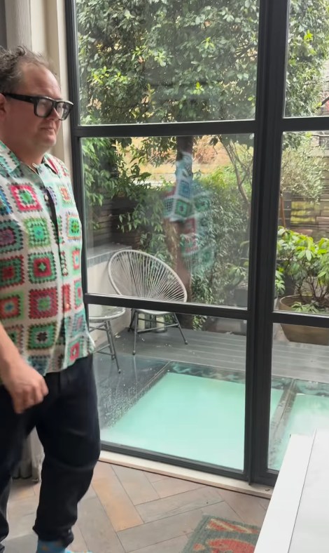 Alan Carr standing by his window which overlooks his terrace garden