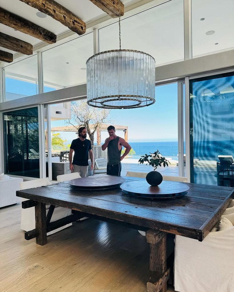 Chris Hemsworth standing with a friend behind the dining room table in his living room at home