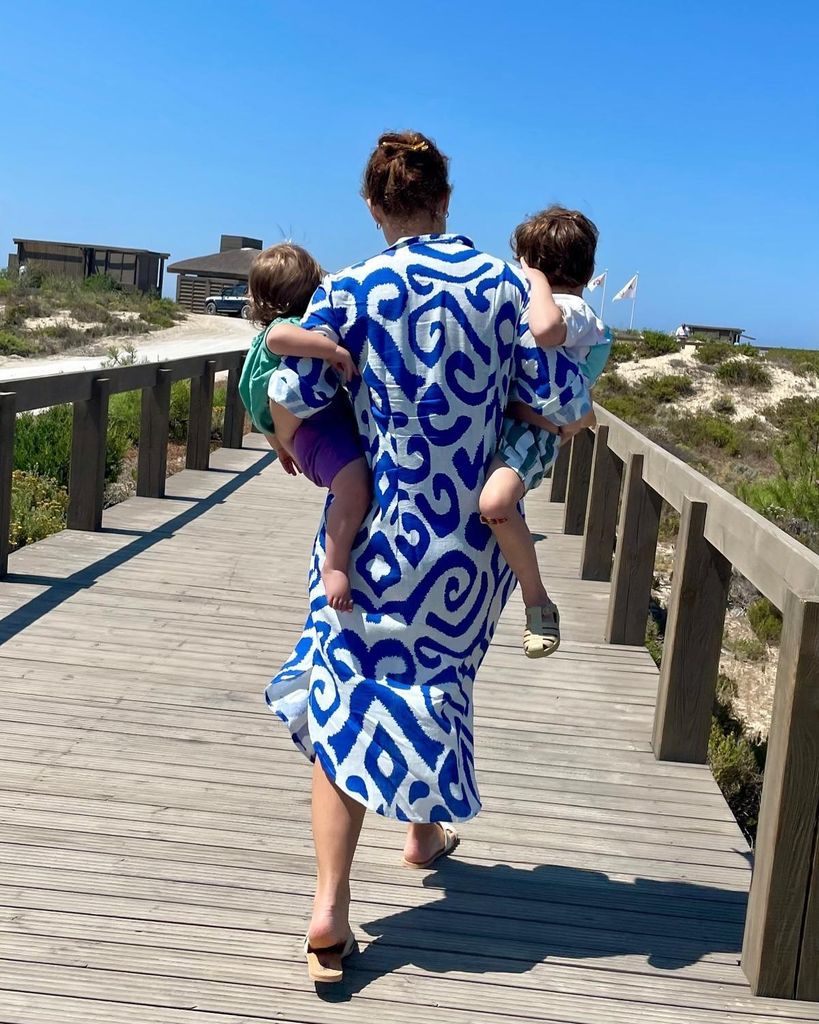 Princess Eugenie in blue and white dress on wooden jetty carrying sons Ernest and August