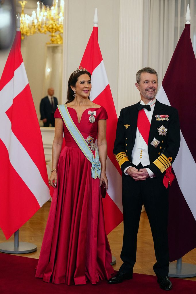 Queen Mary and King Frederik standing in front of flags at Latvia state banquet