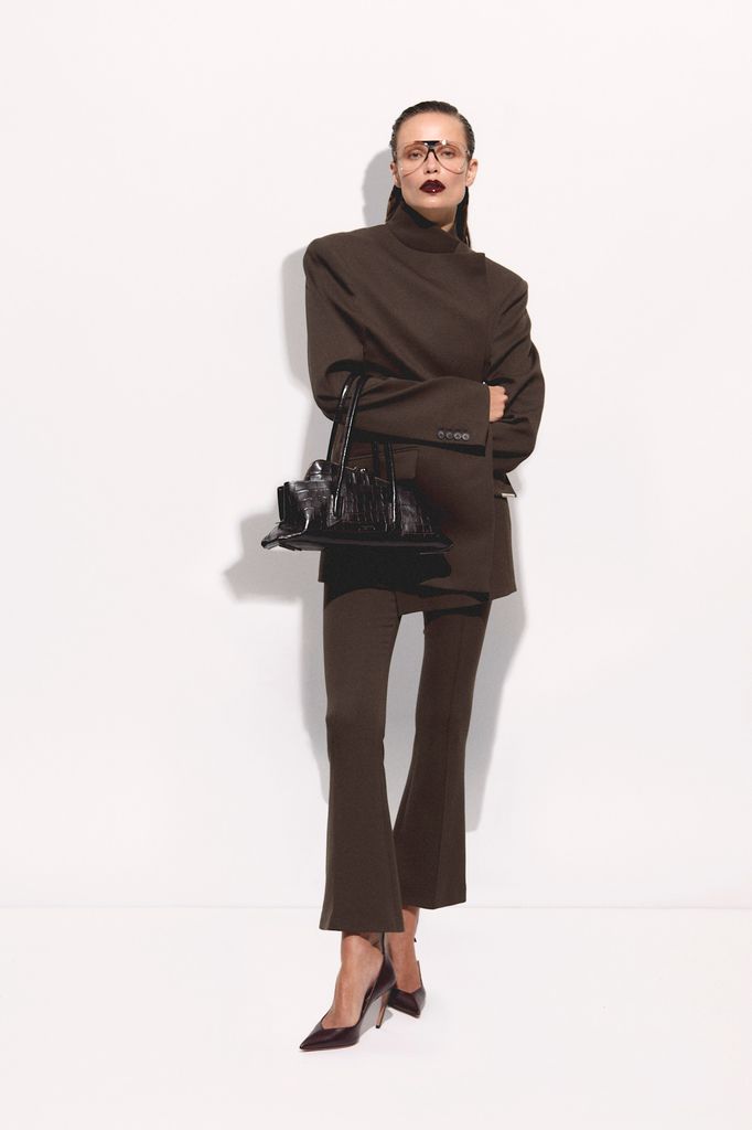 A model poses in a brown high necked jacket and flared cropped trousers in a matching shade