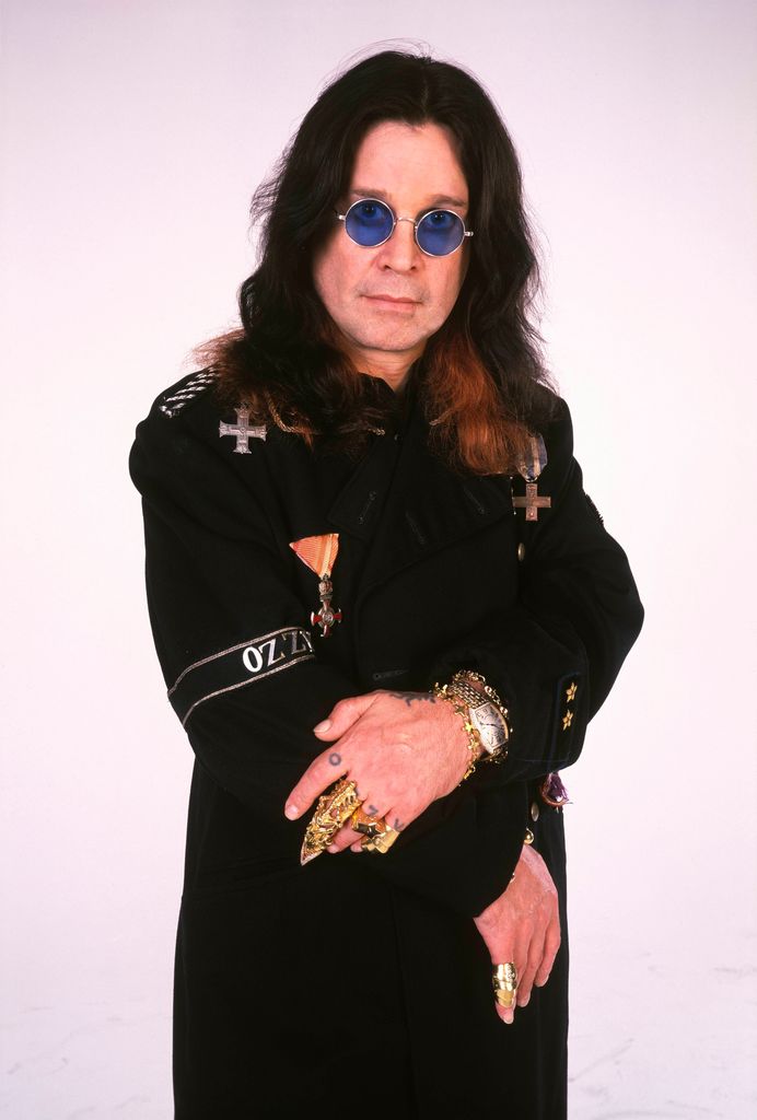 Ozzy Obourne posing in black with his blue tinted sunglasses 