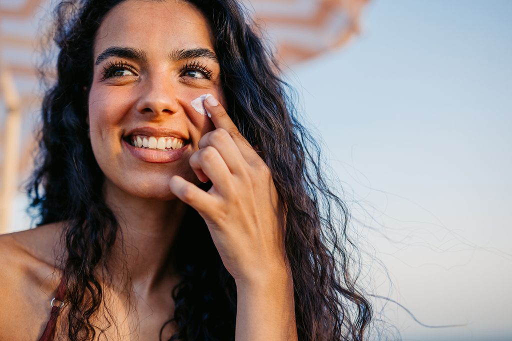 Young woman applying sunscreen on her face while sitting on the beach in Barcelona in Spain.