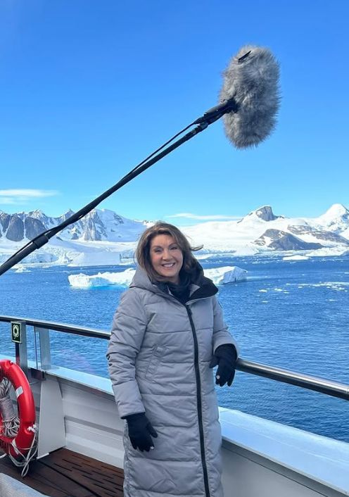 Jane McDonald standing on a cruise ship in a grey parka coat with a boom mic hovering over her