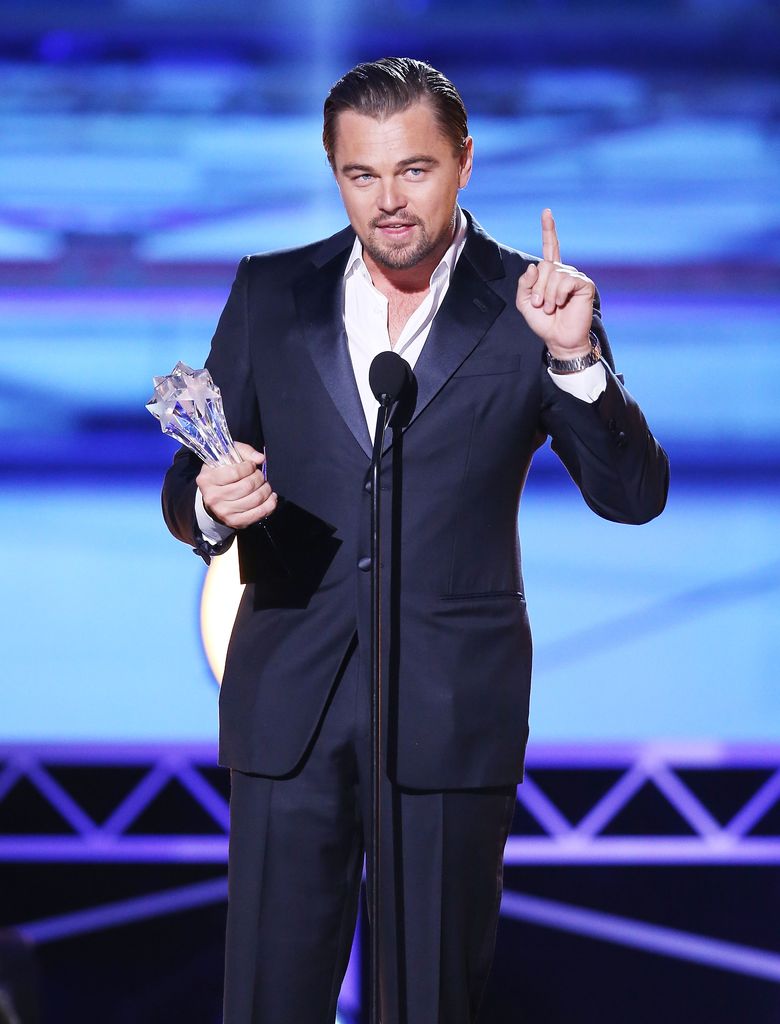 Leonardo DiCaprio makes a speech on stage wearing a navy blue single breasted suit and holding an award