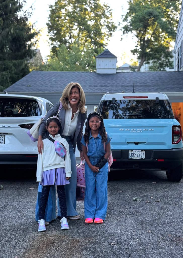 Hoda Kotb in gray blazer and jeans posing outside her house and in front of her cars with her two daughters. 