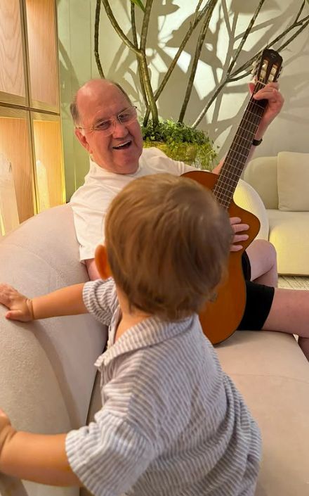 An elderly man playing guitar to a young boy