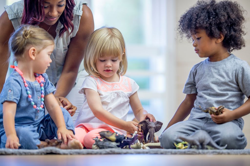 A female daycare provider with some toddlers as they play with toy animals together.