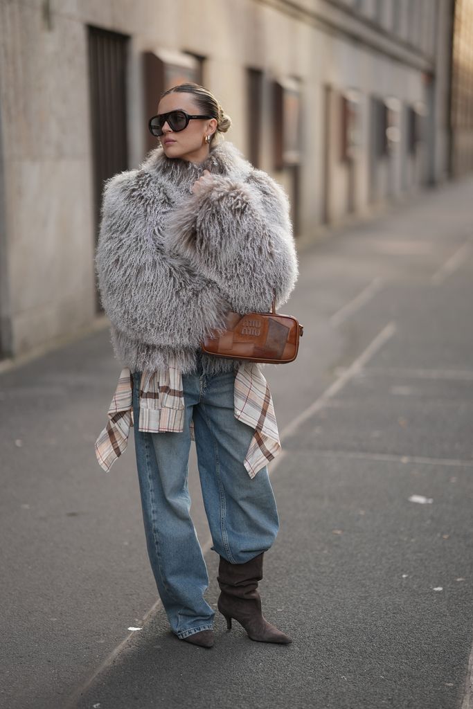 Romina Meier is seen wearing an oversized light grey Rochelle shearling jacket made of mongolian sheepskin with a curly finish, a high collar and plush texture from Ducie London; a beige checkered shirt tied around the waist; wide-leg light blue barrel leg denim pants with a relaxed fit from Massimo Dutti; a pair of grayish dark brown suede boots with pointed toe, slouchy shape and medium high heel from MANGO; a cognac Miu Miu Beau Patchwork leather handbag with patchwork pattern in different brown tones from Miu Miu; acetate sunglasses with an oversized pilot silhouette design in tortoiseshell design from Prada; silver and golden hoop earrings from high by honey hoops, with one in 30mm 18k gold plated and another in 25mm rhodium plated; her blonde hair is styled in a sleek, twisted bun with a center parting on November 10, 2025 in Duesseldorf, Germany.