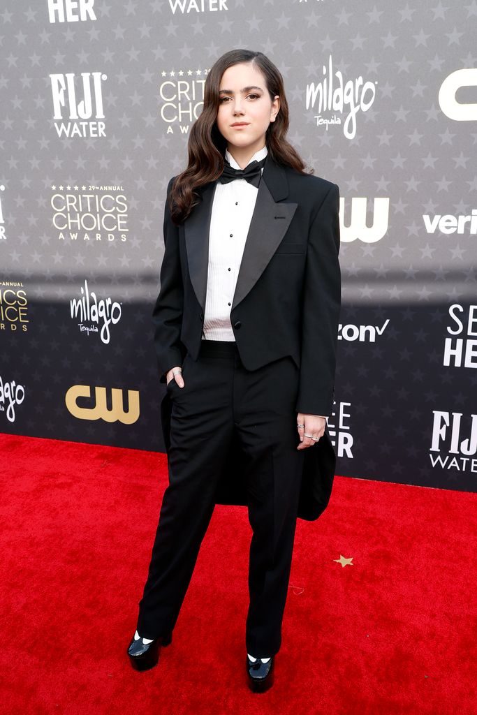 Abby Ryder Fortson weas a tuxedo jacket paired with black trousers, platform shoes a white shirt and black bow tie on the red carpet