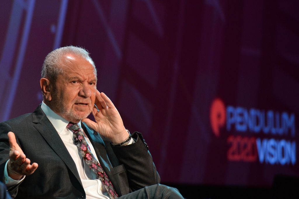 alan sugar speaking on stage in suit and tie 