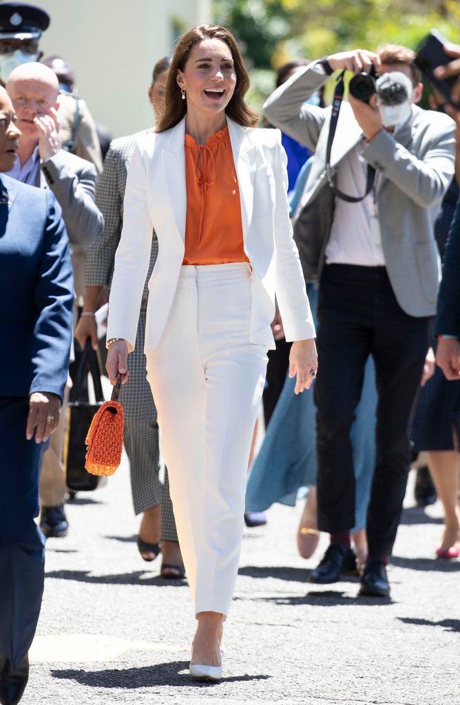 Kate in white suit and keyhole orange blouse walking
