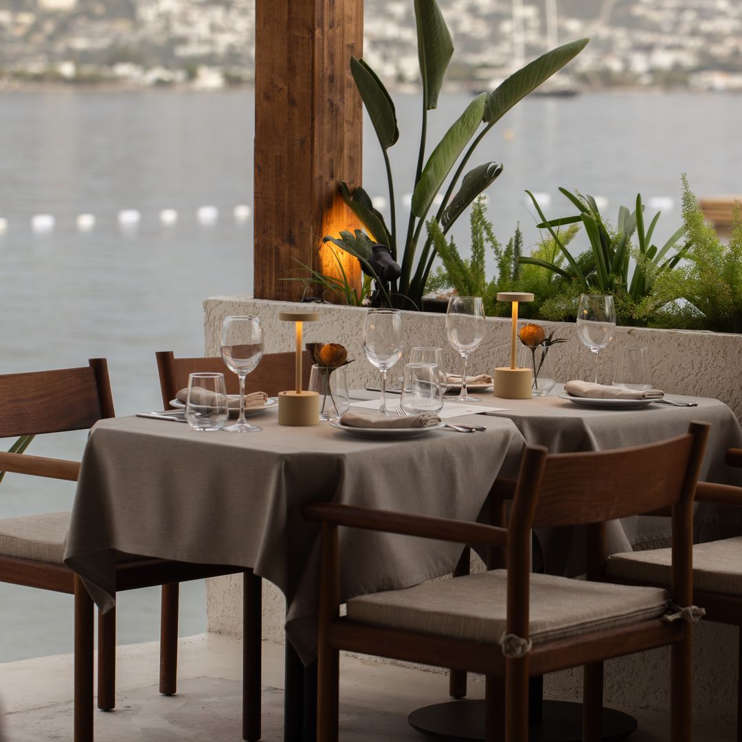 Elegant outdoor dining setup at Avantgarde Refined Bodrum overlooking the sea, with candlelit tables, neutral-toned decor and views across Yalıkavak Bay.