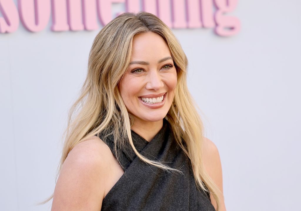 Hilary Duff smiles at the camera in a wrap over halter-neck dress.