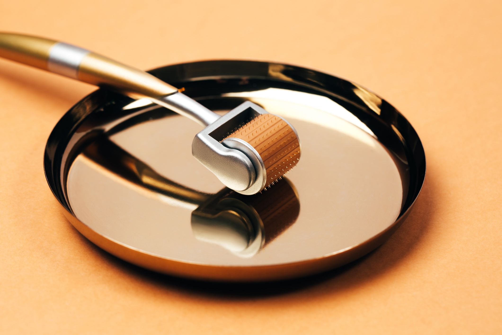 Metal silver-orange massage roller with microneedles on pastel orange background. Concept of dermatological treatment of different skin conditions. Macro photography