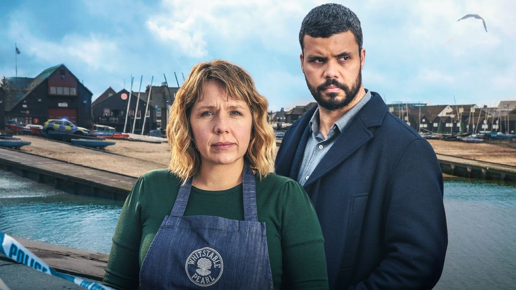 woman in apron next to man in suit by harbour