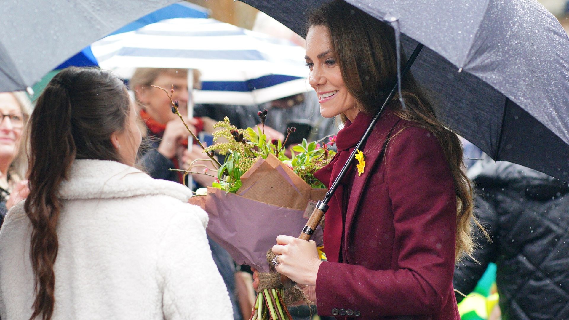 Kate Middleton holding an umbrella and a bouquet of flowers