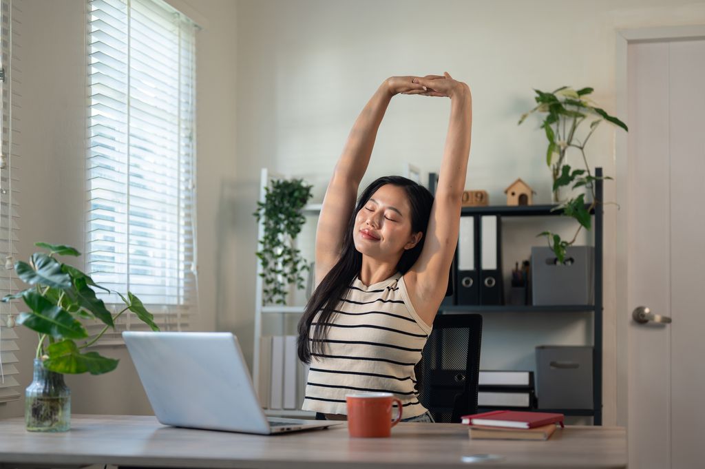 A beautiful, carefree Asian businesswoman is stretching her arms to relax after finishing her work on a laptop, working in her office