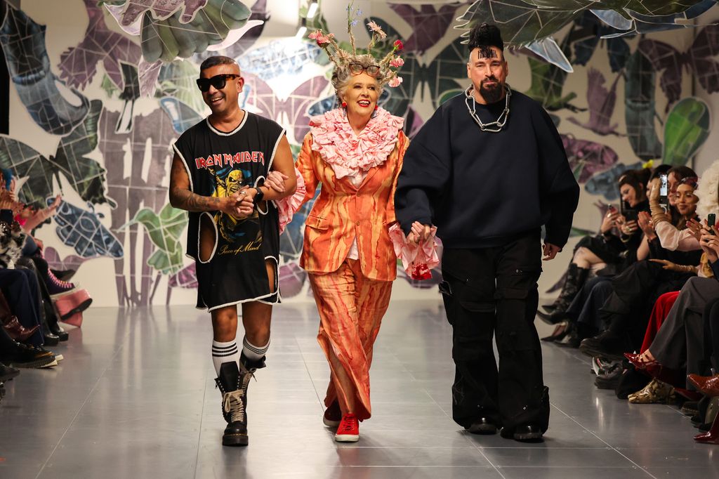 A photo of Prue Leith walking down a catwalk with fashion designers Omi and Vin