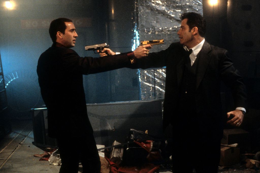 John Travolta and Nicholas Cage aim guns at one another.