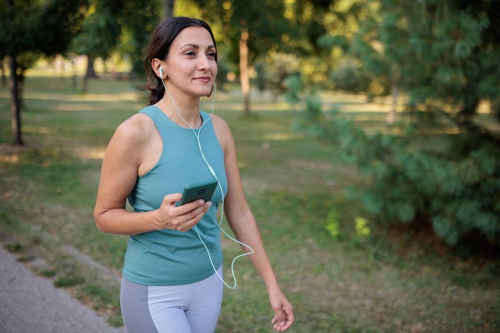 A mid adult woman listening to music while walking in a public park