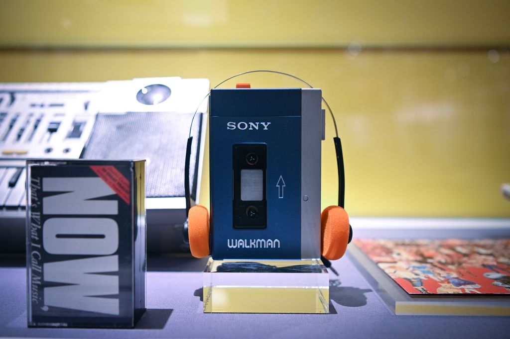 Original Sony Walkman shown with orange headphones in an exhibition case.