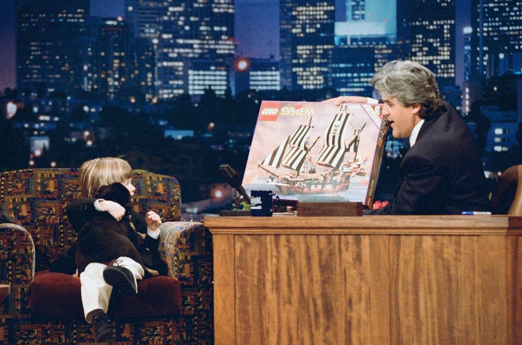 Host Jay Leno holds up a Lego System ship with striped sails to actor Haley Joel Osment during an interview.